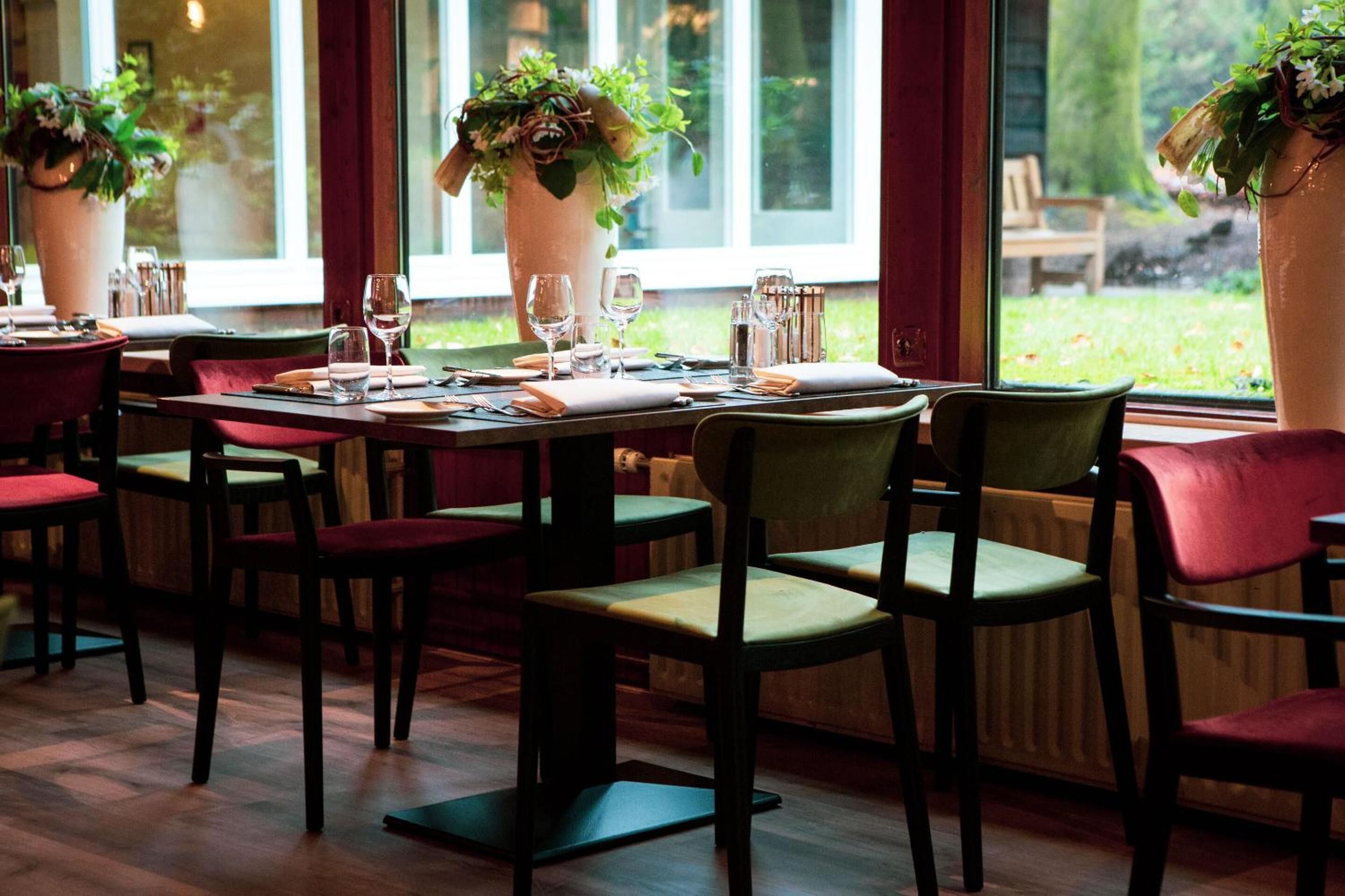 A restaurant with tables set for dining, chairs, and potted plants.