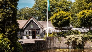 A traditional building with a thatched roof, a brick wall, and a small pond with lily pads. - De Lunterse Boer (Lunteren)