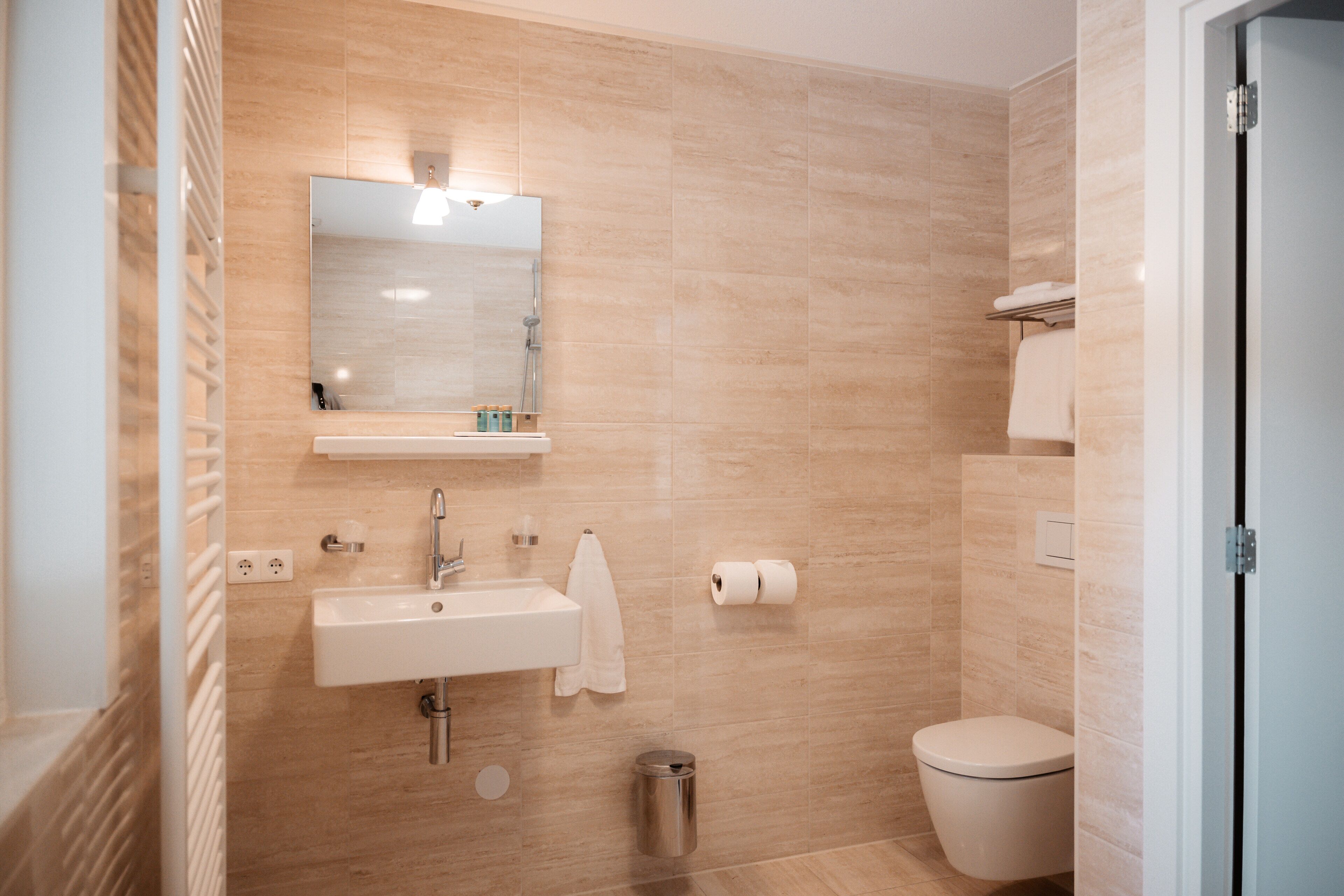 A modern bathroom with a sink, mirror, toilet, and a trash bin.
