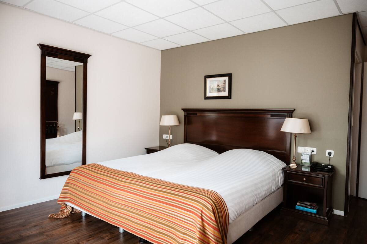 Ein Hotelzimmer mit einem großen Bett, zwei Nachttischen mit Lampen, einem Spiegel und einem gerahmten Bild an der Wand.