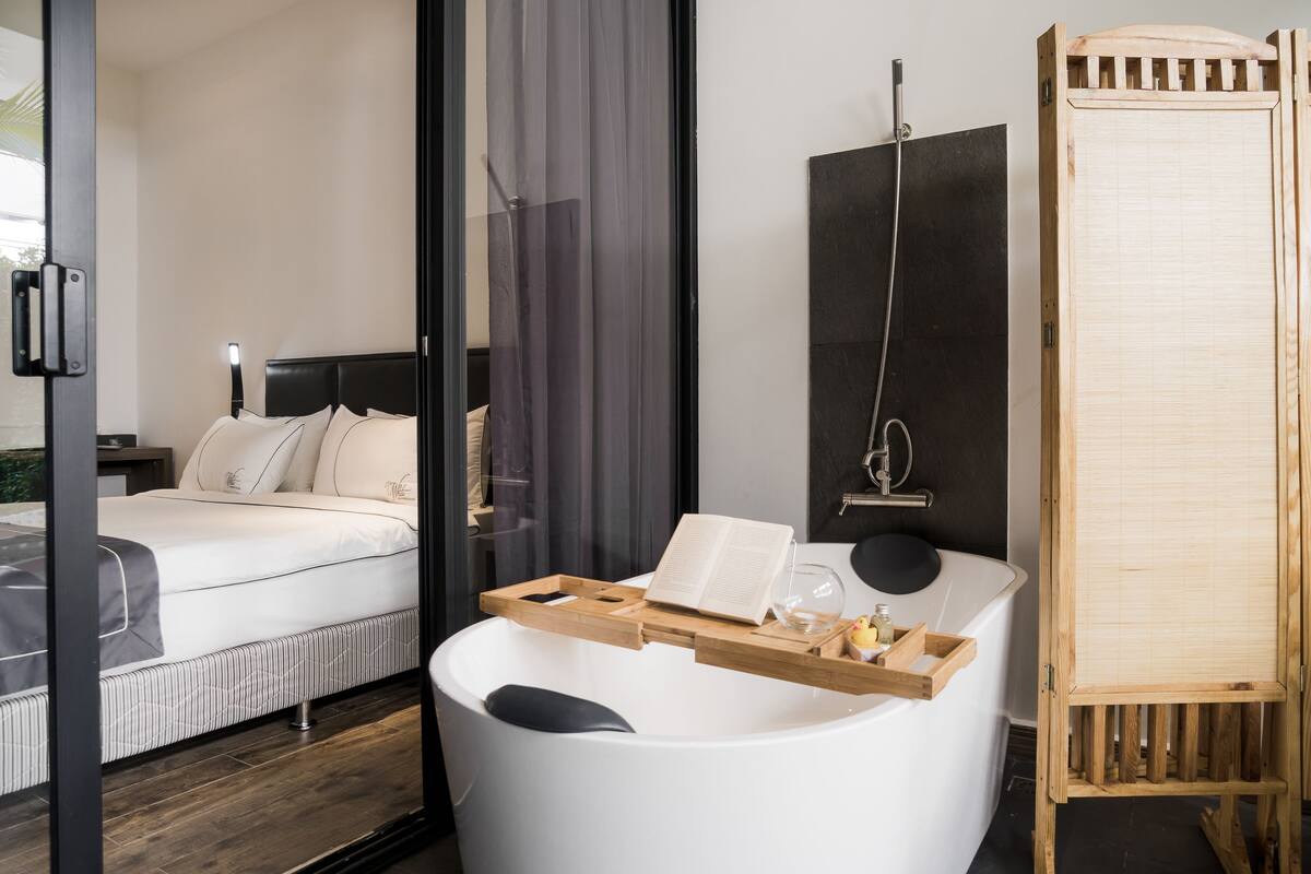 Una habitación de hotel moderna con una cama grande, una bañera y un armario de madera.