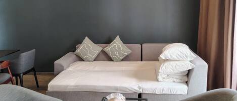 A modern hotel room with a sofa bed, a glass coffee table, and two armchairs.