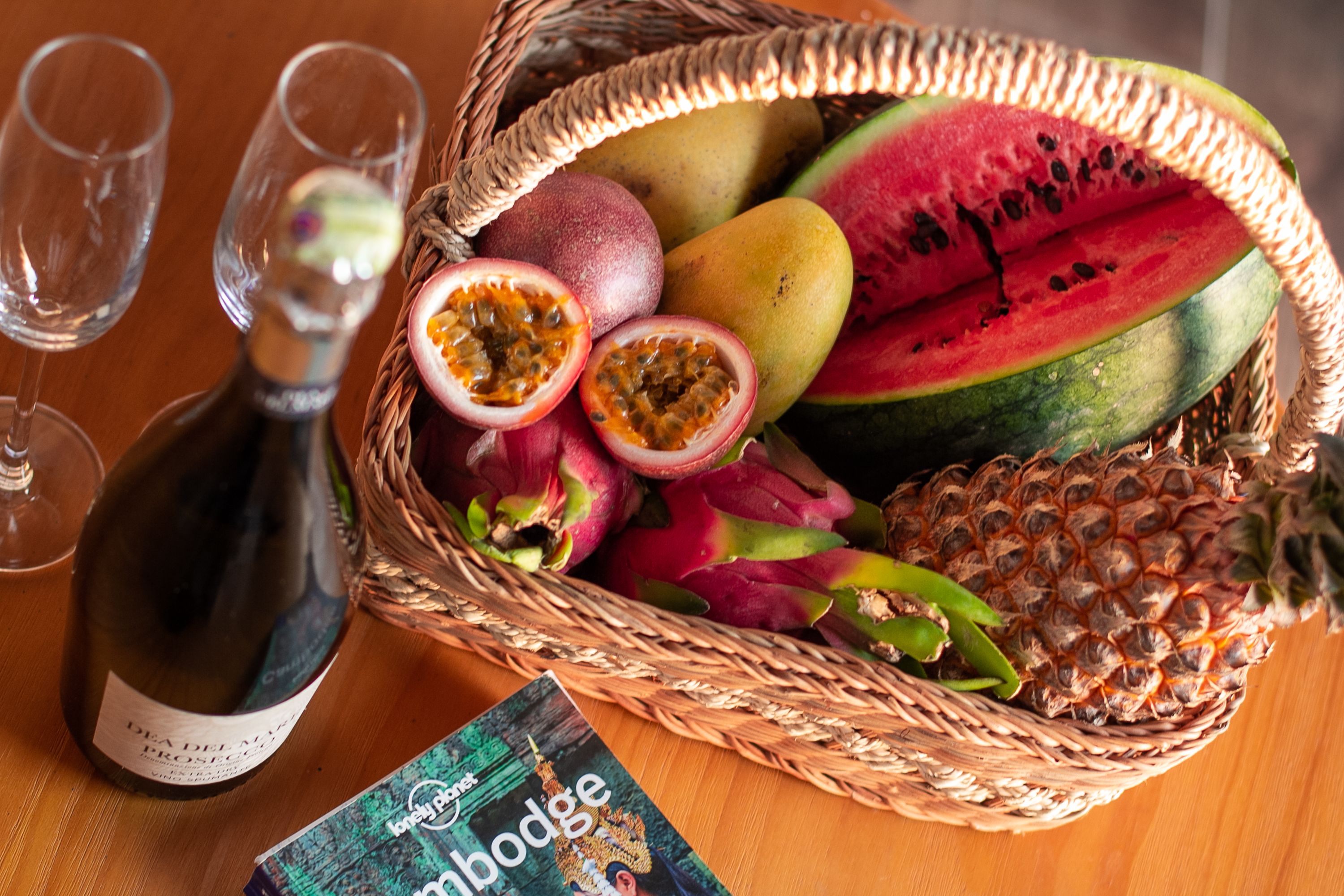 A wicker basket filled with fruits and a bottle of wine on a wooden table.