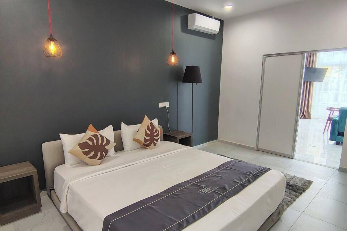 Un dormitorio moderno con una cama grande, dos mesitas de noche, una lámpara de pie y una puerta corredera que da a otra habitación.