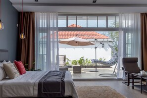 Un dormitorio moderno con una cama grande, un balcón con mesa y sillas, y vista a un tejado de tejas rojas.
