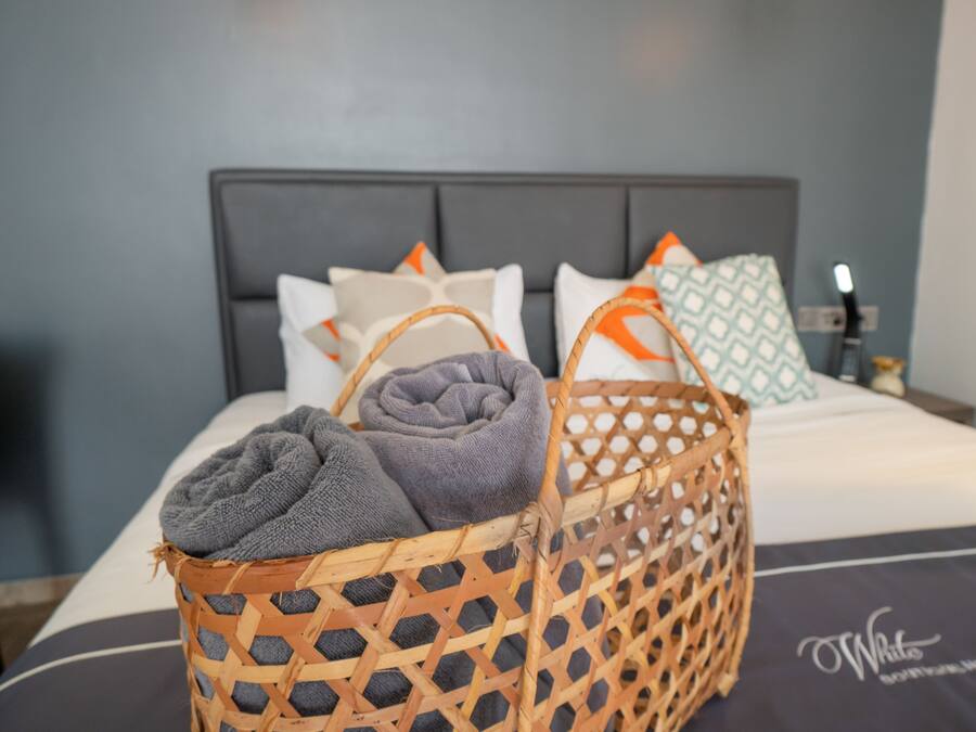 Een net opgemaakt bed met een grijs-wit gestreept laken, een grijze handdoek en een rieten mand met een grijze handdoek.