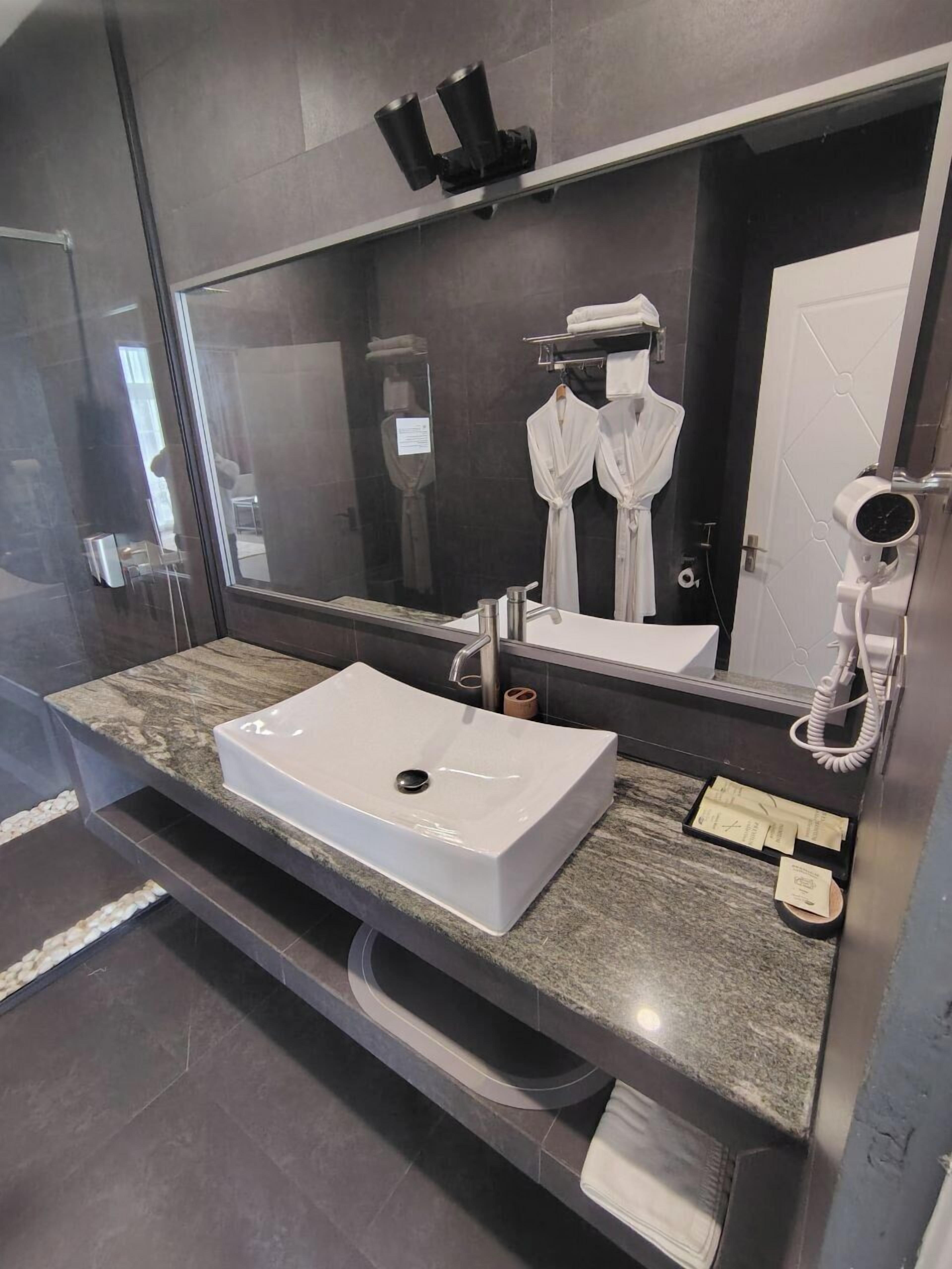 Une salle de bain moderne avec un grand miroir, un lavabo blanc, un porte-serviettes et un sèche-cheveux.
