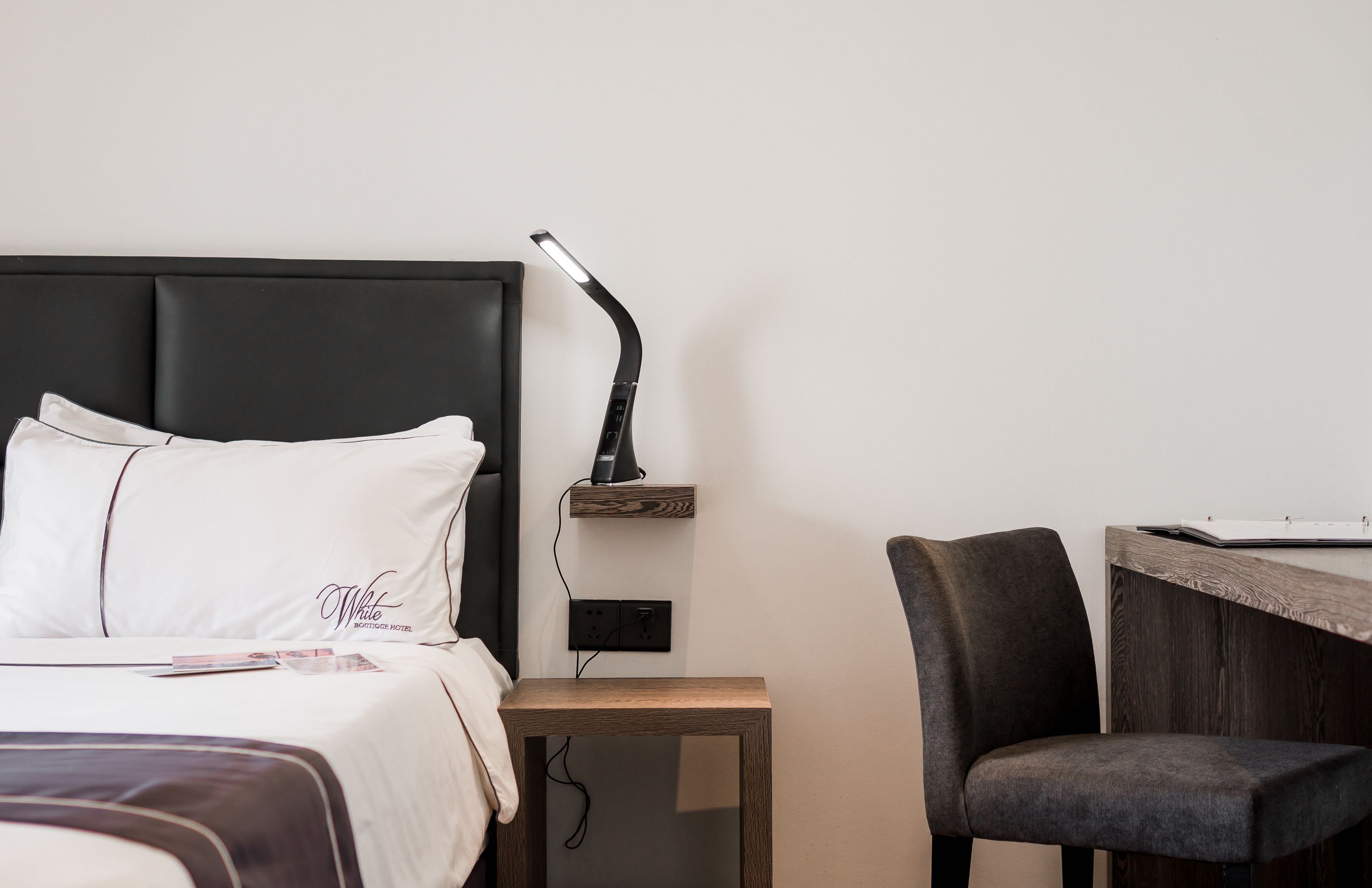A neatly arranged hotel room with a bed, bedside table, lamp, and a chair.