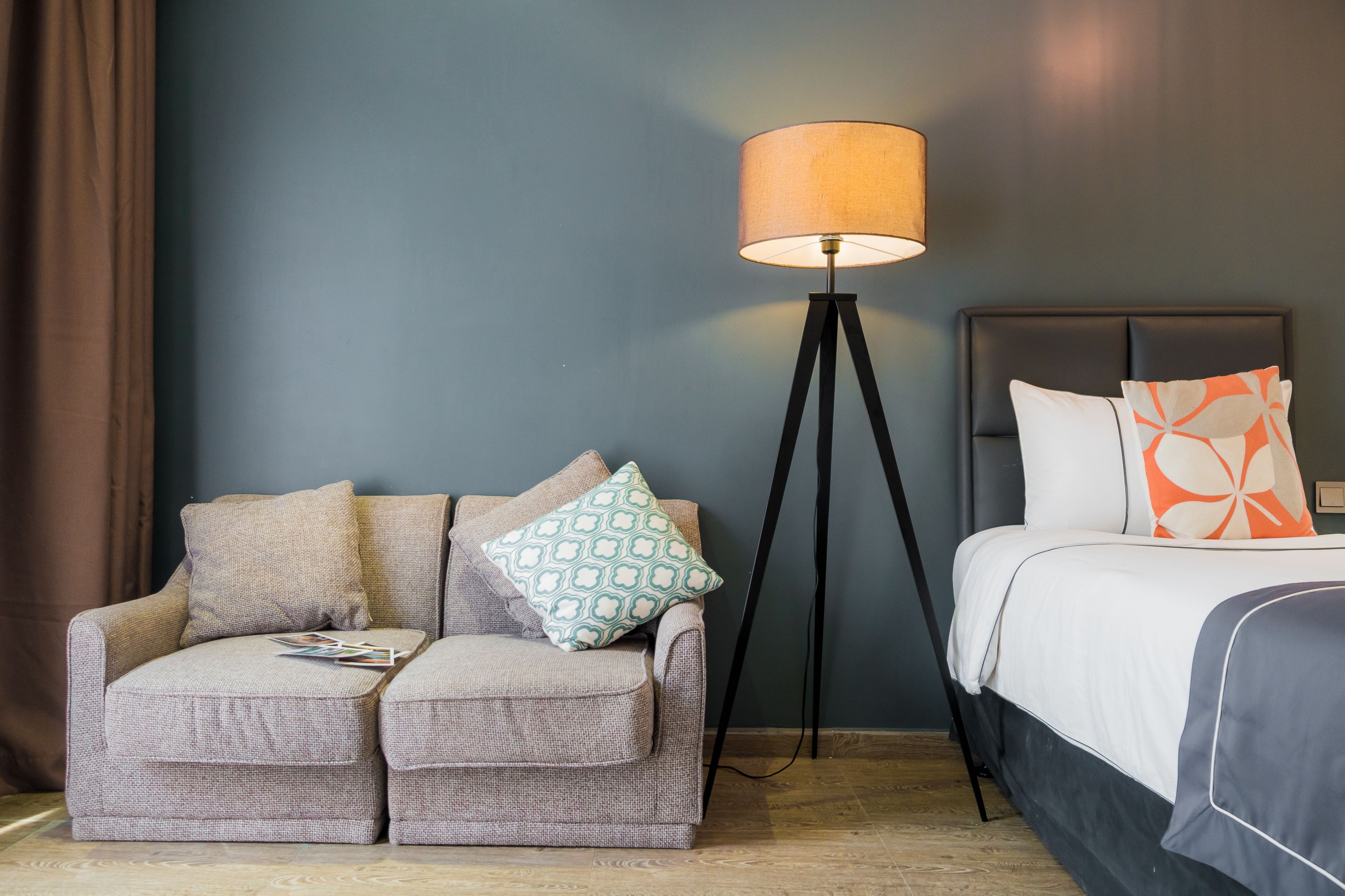 A hotel room with a sofa, a floor lamp, and a bed with patterned pillows.