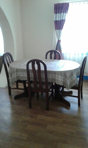 A dining area with a round table, four chairs, and a patterned tablecloth.
