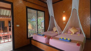 Habitación con dos camas, cada una con dosel, suelo de madera y una ventana con persianas.