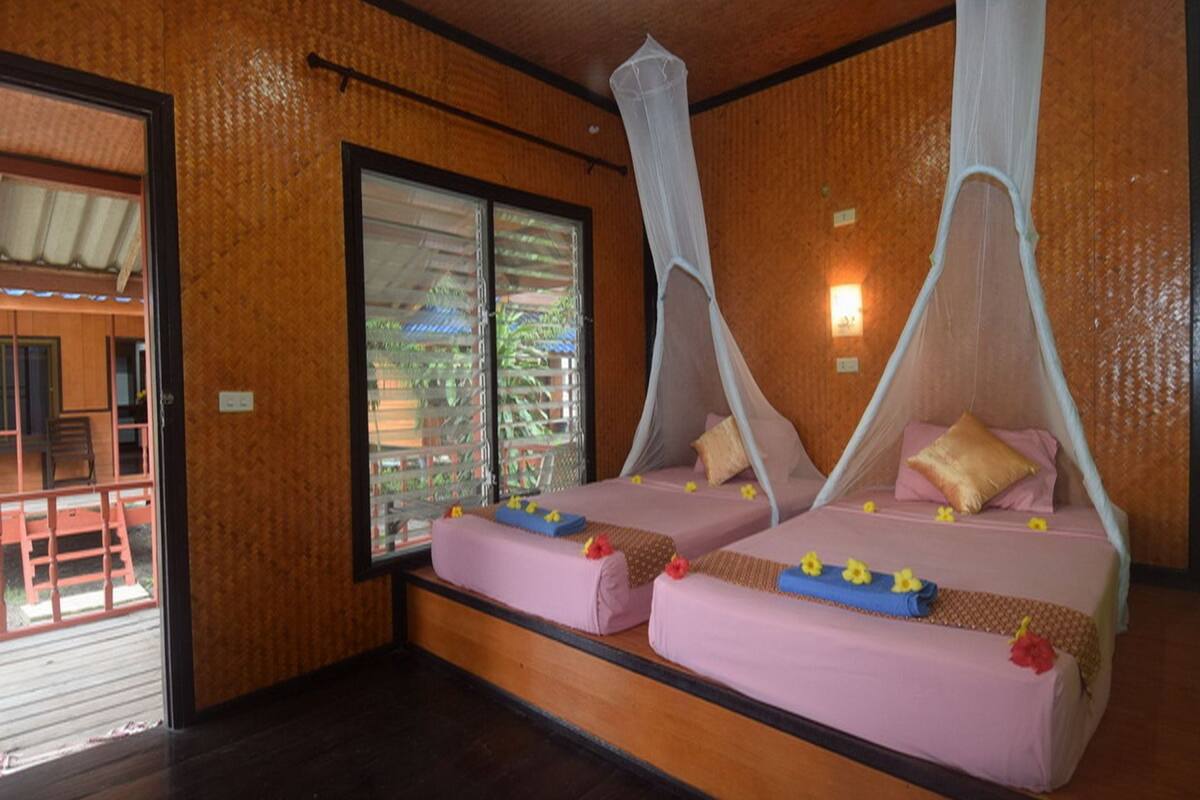 Ein Zimmer mit zwei Betten, jeweils mit Baldachin, Holzboden und einem Fenster mit Jalousien.