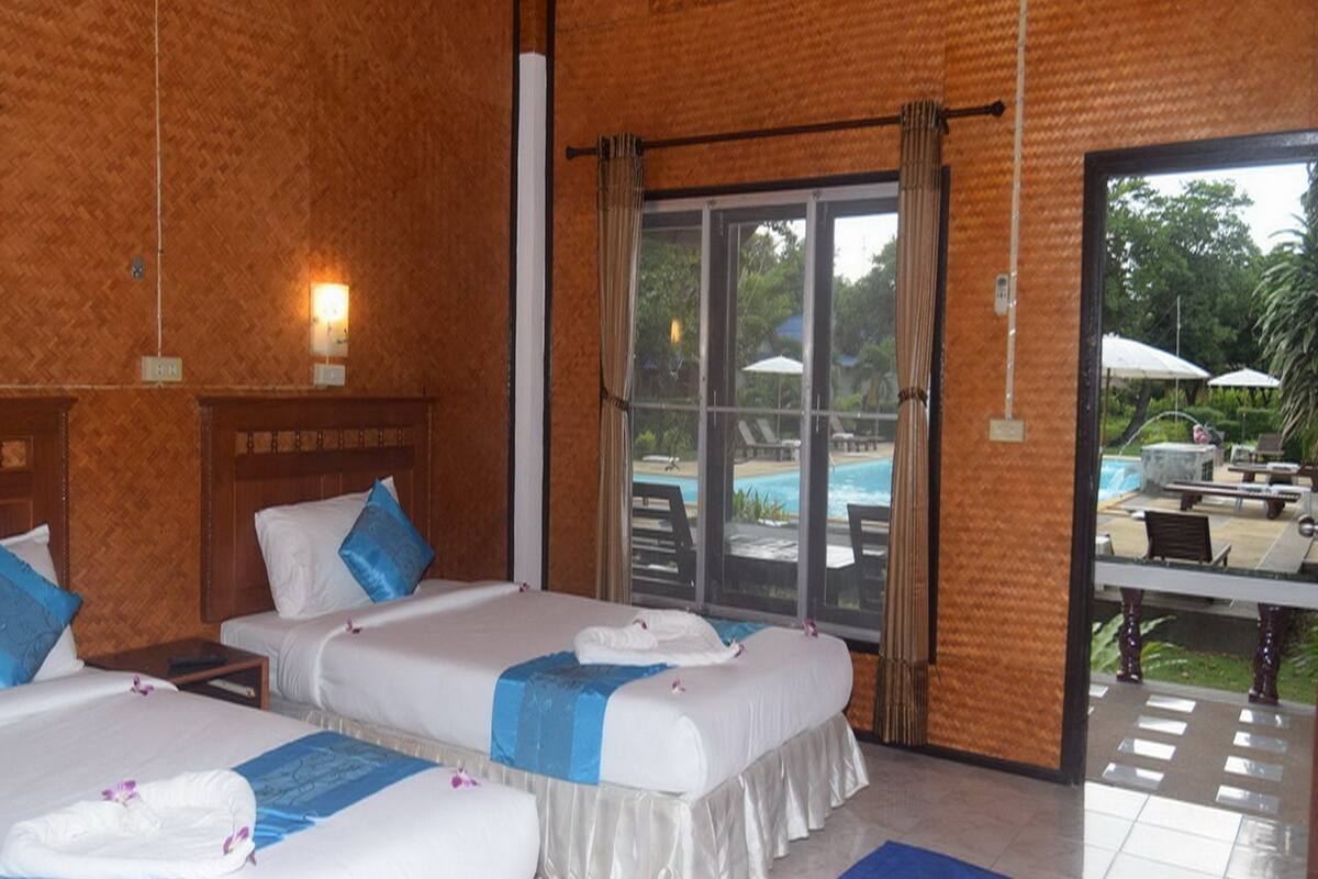 Ein Hotelzimmer mit zwei Betten, einem großen Fenster mit Blick auf einen Pool und Sitzgelegenheiten im Freien, sowie einer Wand mit Holzstruktur.
