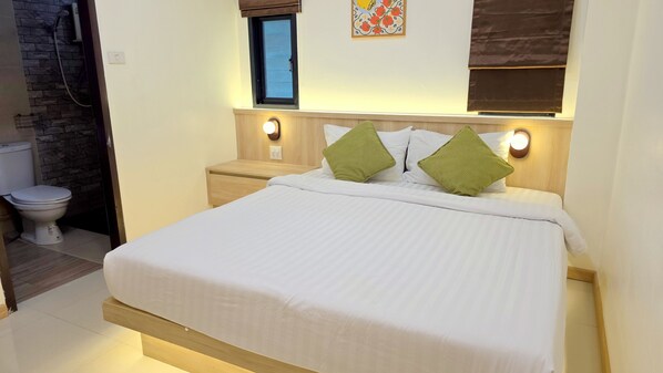 A hotel room with a bed, a nightstand, a wall-mounted light, a window, and a toilet. - Samed Port View (Rayong)