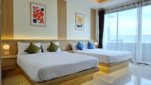 Een hotelkamer met twee bedden, elk voorzien van wit beddengoed en blauw-groene kussens. Op de muren hangen bloemrijke kunstwerken in lijsten, er is een groot raam met gordijnen en een houten hoofdbord.