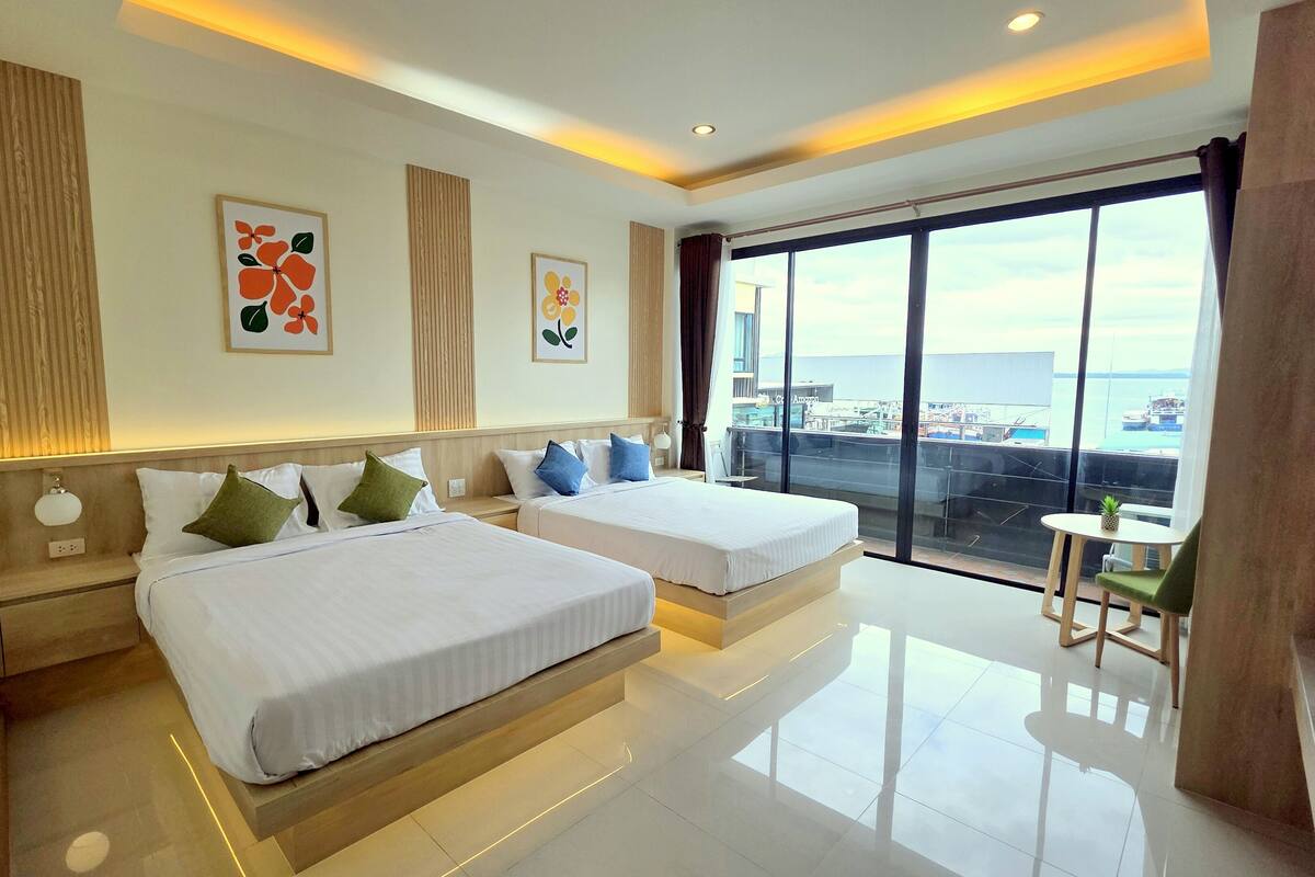 Habitación de hotel con dos camas, un balcón con vista al mar y obras de arte en las paredes.