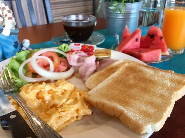 Une assiette de petit-déjeuner comprenant des œufs brouillés, des toasts, des tomates, des oignons et un verre de jus d’orange.