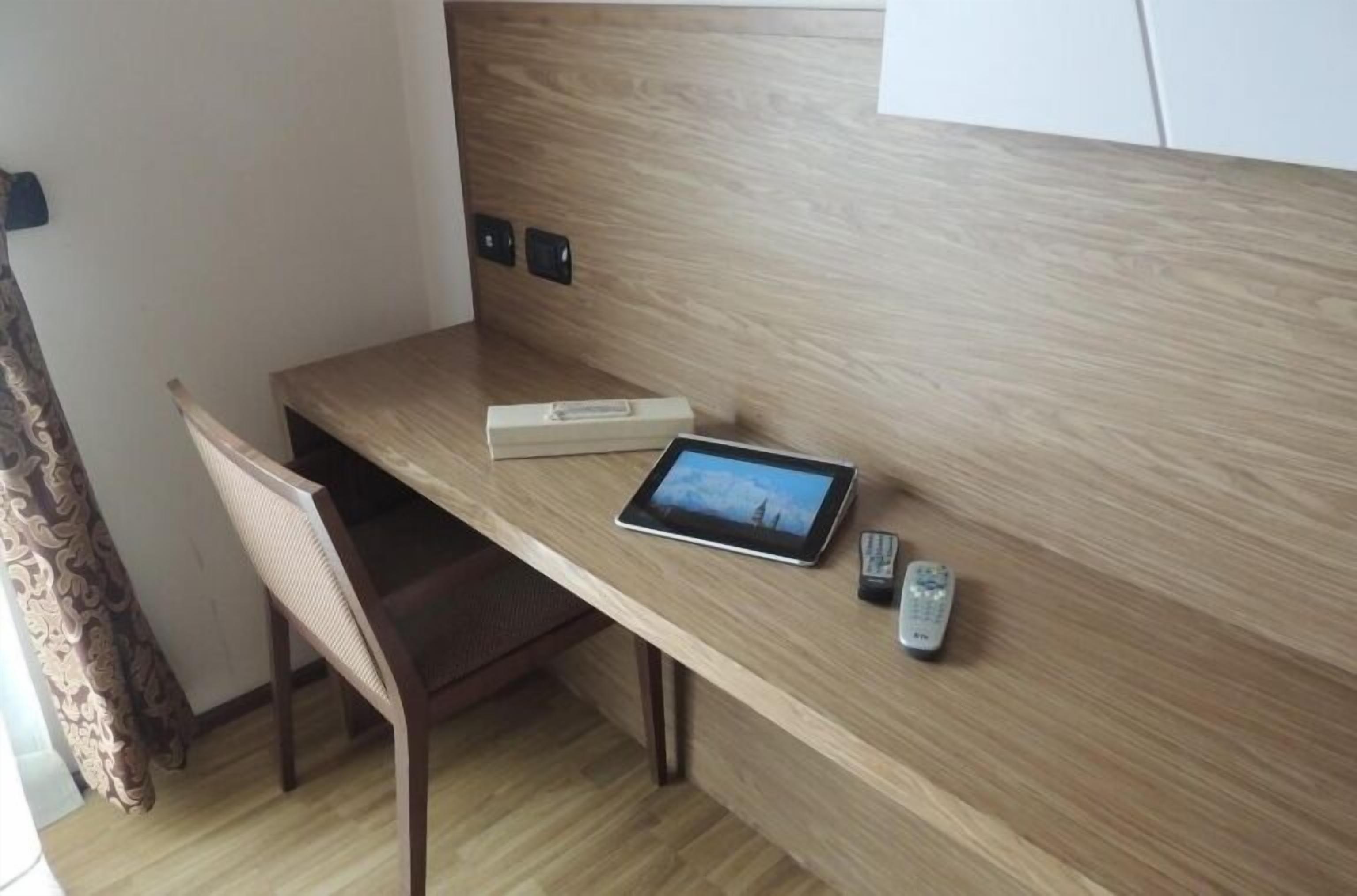 Una scrivania in legno con un tablet, un telecomando e una scatola.