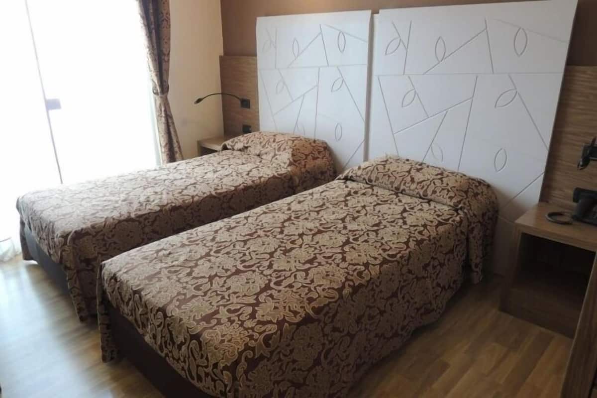 A room with two beds, patterned bedding, a wooden floor, and a geometric wall design.