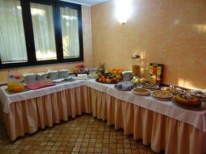 A buffet table with various food items and beverages, set against a wall with a window.