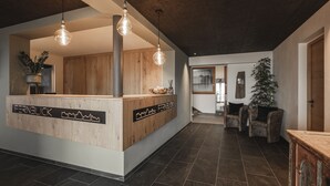 A reception area with a wooden counter, pendant lighting, and a view into a living area with a couch and a plant. - Hotel Fernblick (Bressanone)