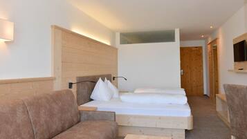 Una habitación de hotel moderna con cabecera de madera, cama con ropa blanca, sofá marrón y televisor de pantalla plana montado en la pared.