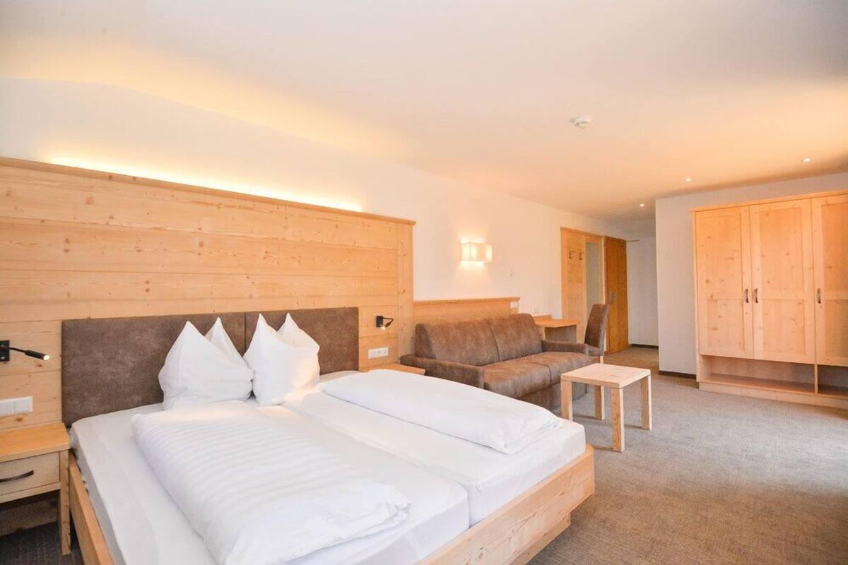 Ein modernes Hotelzimmer mit einem großen Bett, einer Couch, einem kleinen Tisch und Holzkästen.