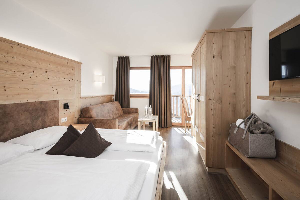 Ein Hotelzimmer mit zwei Betten, einem Sofa, einem Fernseher und einem Balkon mit Vorhängen.
