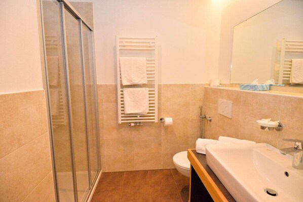 Un baño con cabina de ducha de vidrio, inodoro, lavamanos y toallero con dos toallas.