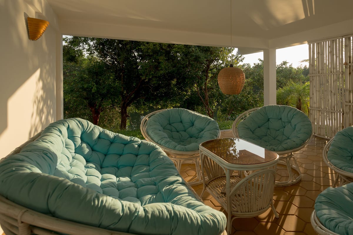 Un espace extérieur abrité, aménagé avec quatre fauteuils confortables et une table, le tout entouré d’une clôture en bambou et d’arbres.