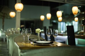 Un ambiente de restaurante con una larga mesa dispuesta para comer, que incluye varios vasos de vino, platos y un jarrón con un arreglo floral.