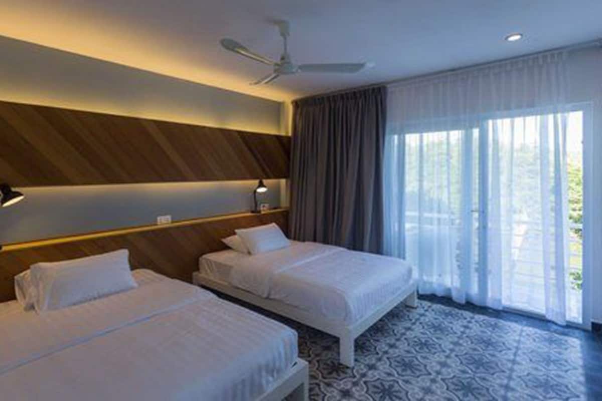 Une chambre d’hôtel avec deux lits, un ventilateur de plafond, une grande fenêtre avec des rideaux et une moquette à motifs.