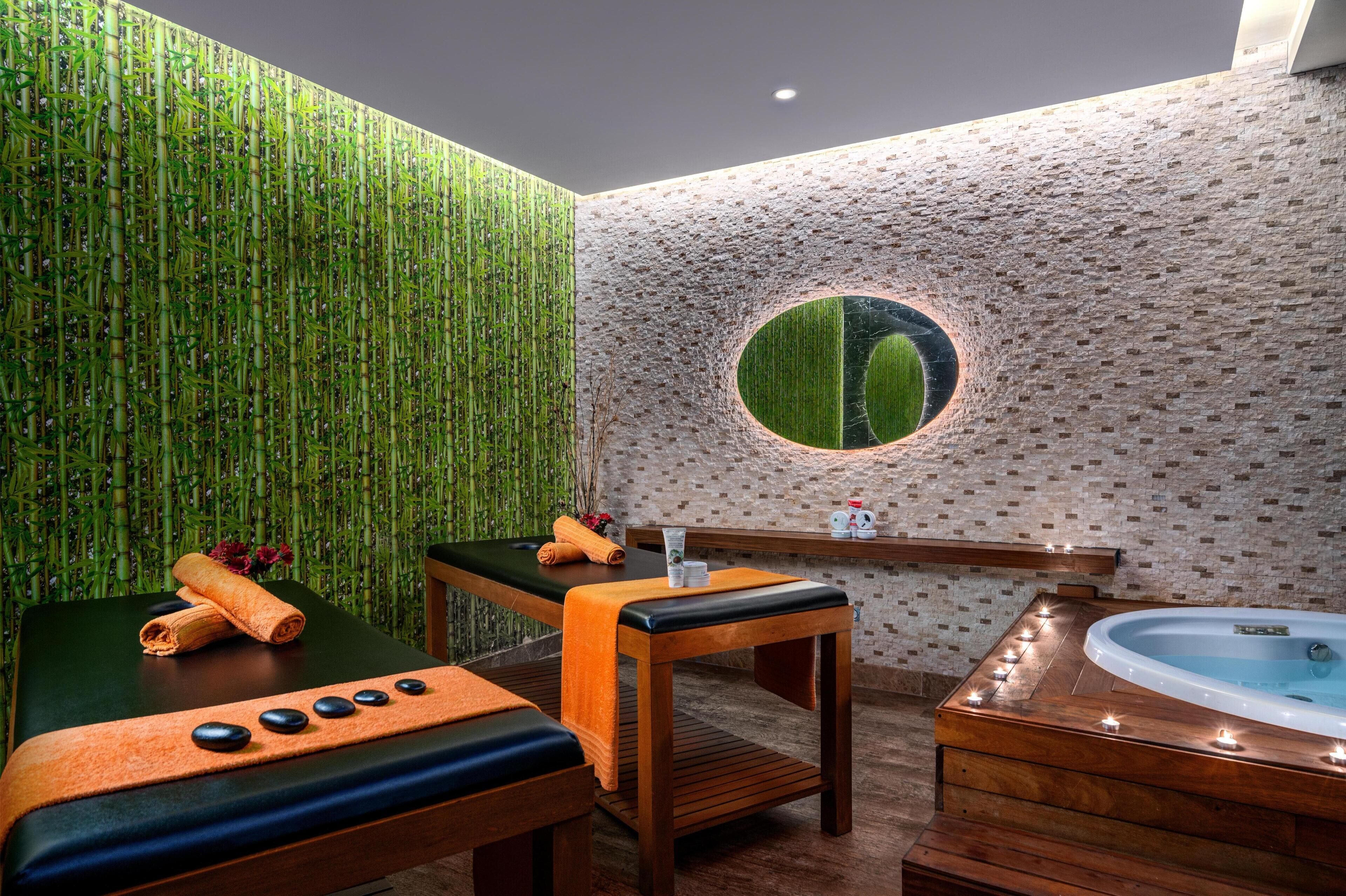 Een spa-ruimte met een massagetafel, een houten bankje, een jacuzzi en een muur met een ronde spiegel.
