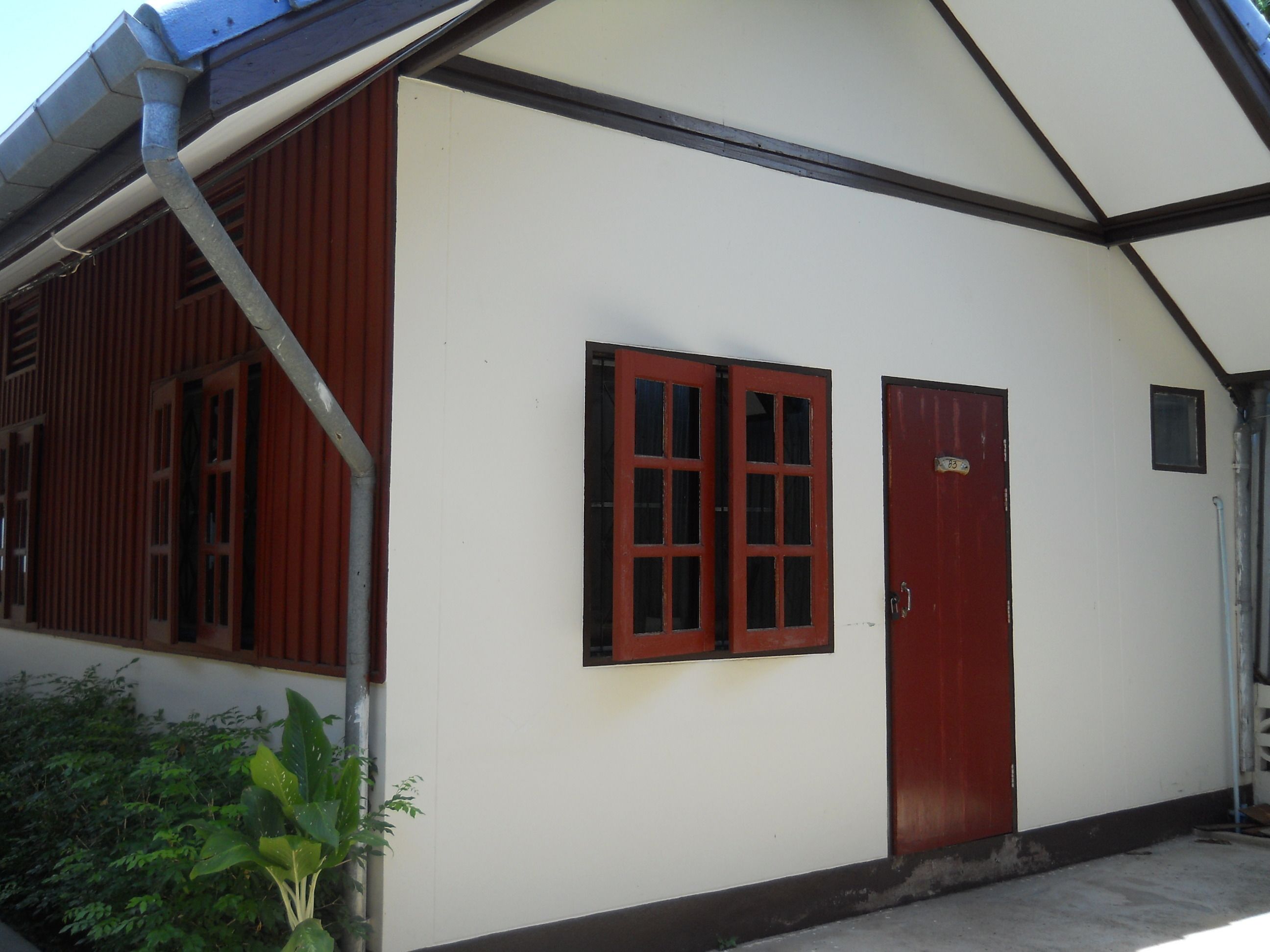 A building with a red door and windows, a white wall, and a metal gutter.
