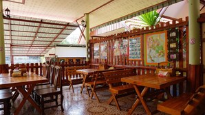 A restaurant with wooden tables and chairs, a tiled floor, and a ceiling with a patterned design. - 4T Guesthouse (Sukhothai)