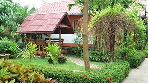 A bungalow with a red roof, surrounded by lush greenery and a garden. - 4T Guesthouse (Sukhothai)