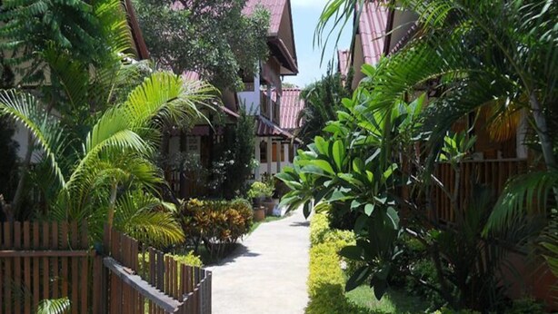 A pathway flanked by wooden fences and lush greenery leading to traditional-style buildings. - 4T Guesthouse (Sukhothai)