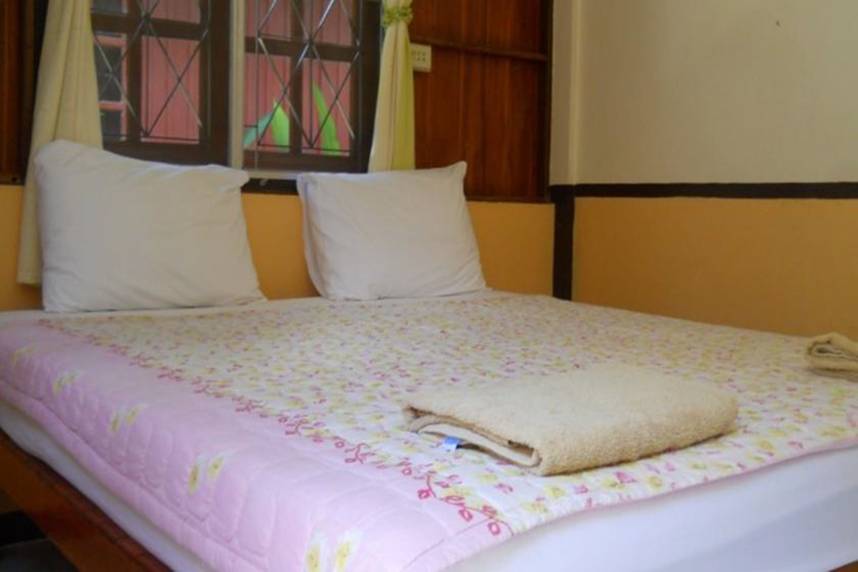 A bed with a floral bedspread, two white pillows, and a folded towel on the bed.