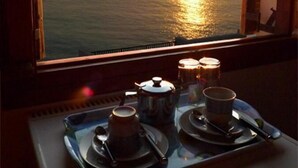 A tray with teapots and cups on a windowsill, overlooking a sunset over the ocean. - Pension Mylos (Agios Nikolaos)