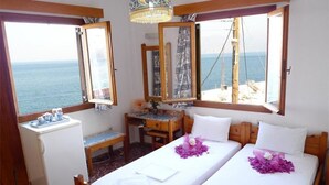 A room with two beds, a desk, a small fridge, and large windows with a view of the sea. - Pension Mylos (Agios Nikolaos)