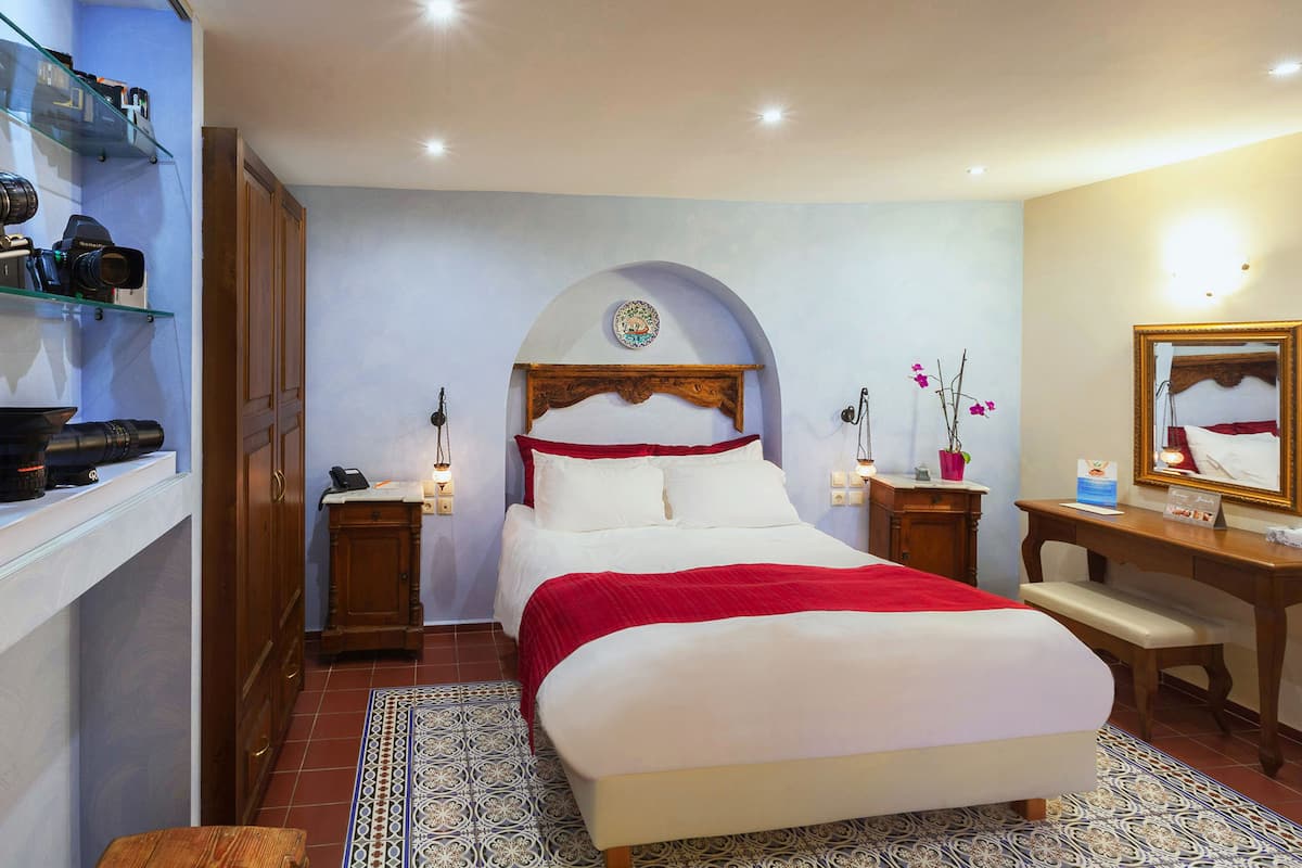 A bedroom with a bed, wooden cabinets, a desk, and a mirror.