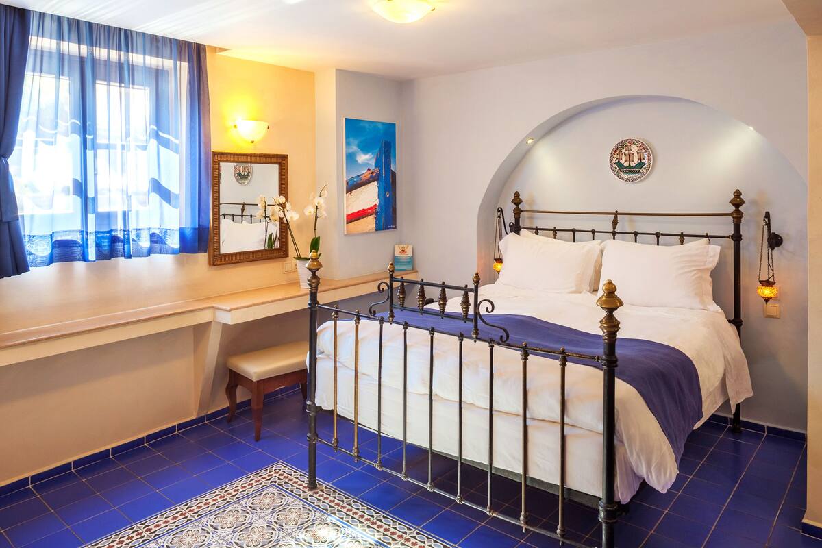 A hotel room with a bed, a bench, a desk, and a view of the sea.