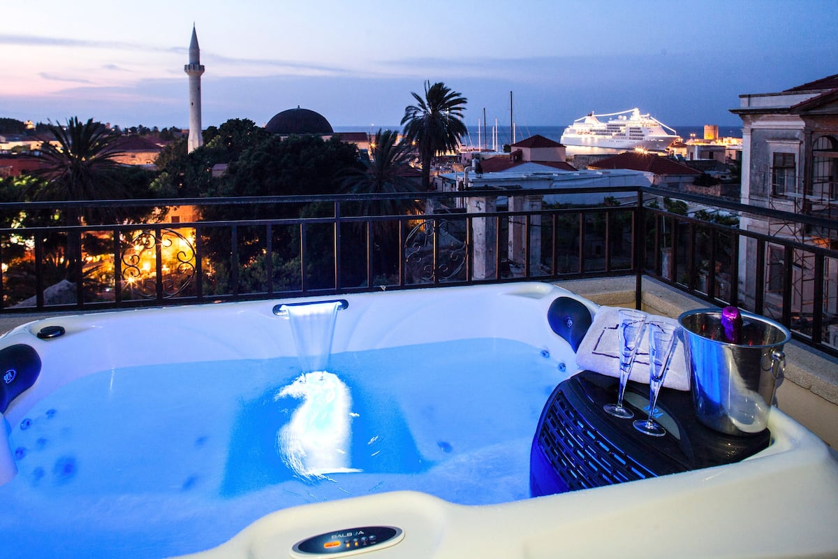 A hot tub with a control panel, two glasses, and a bucket on a balcony with a cityscape view.
