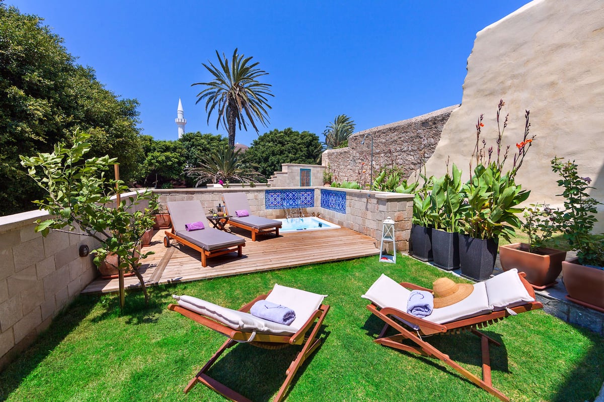 A backyard with two lounge chairs, a hot tub, and a stone wall.