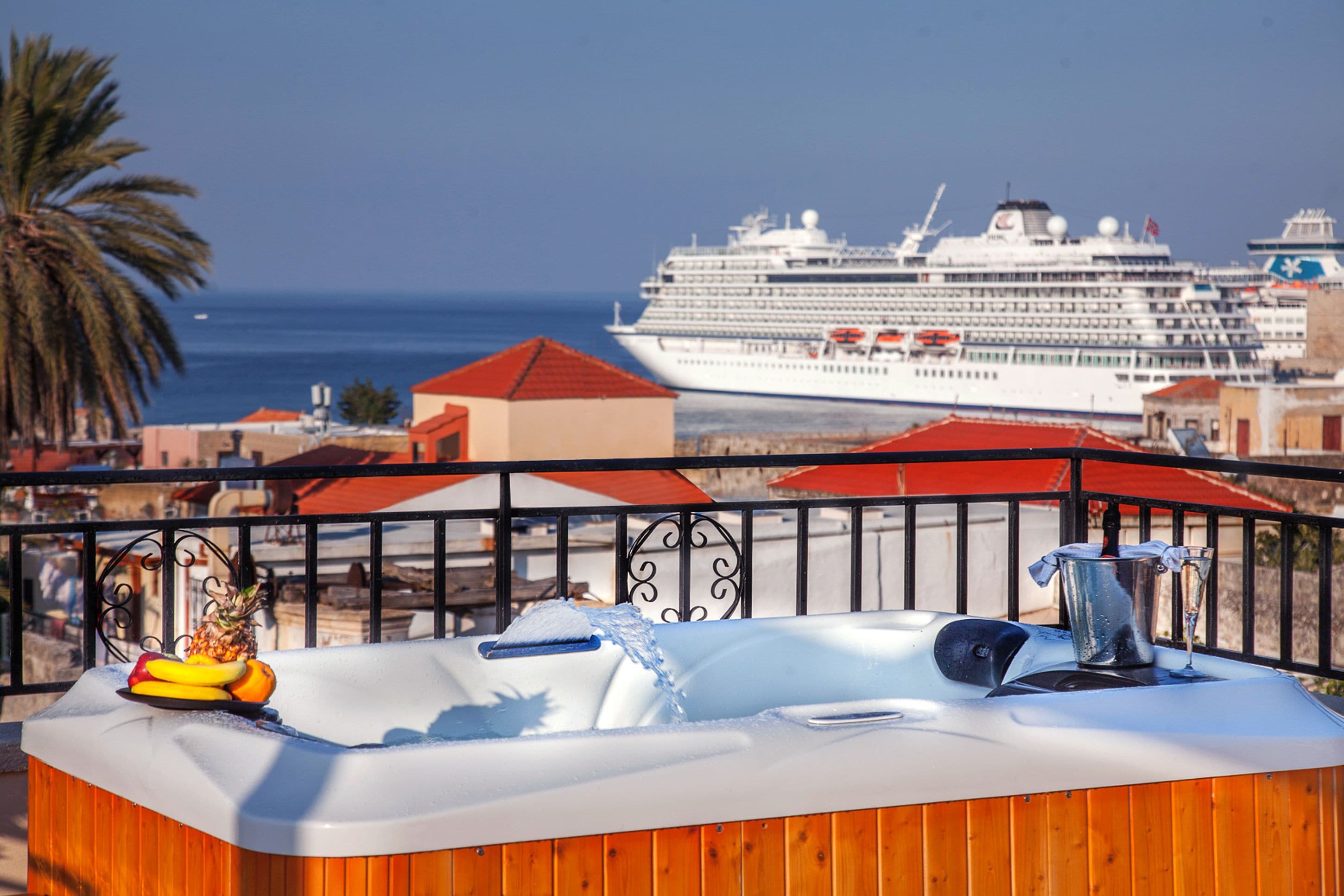 Ein Whirlpool mit Ananas und Bananen auf einer Holzterrasse, mit Blick auf ein Kreuzfahrtschiff und den Ozean.