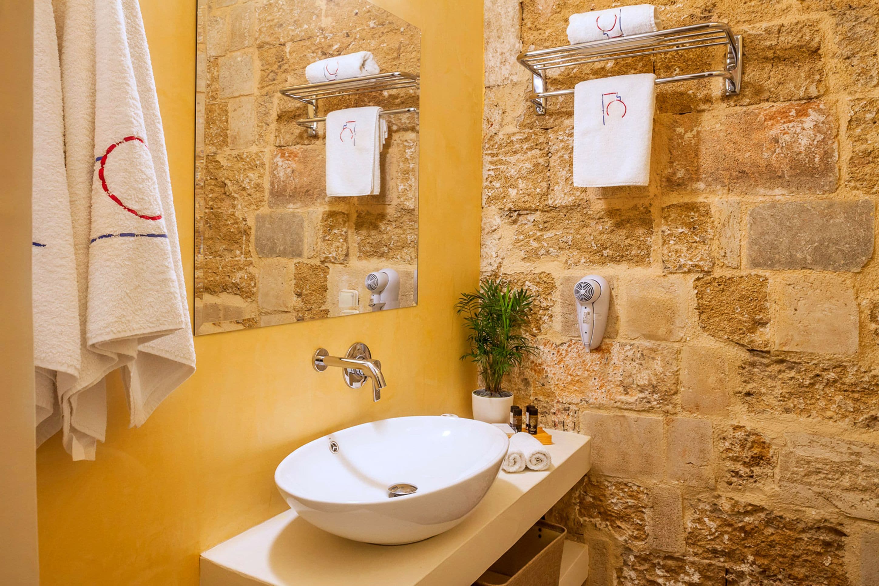 A bathroom with a stone wall, a white sink, and a towel rack.