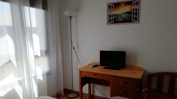 Un dormitorio con una cama, un escritorio con televisor, una silla, una lámpara de pie y un cuadro en la pared.