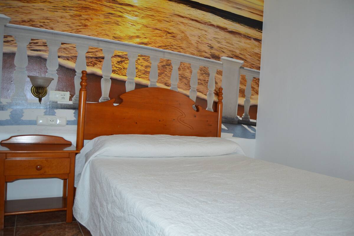 A bedroom with a wooden bed, a nightstand, and a wall-mounted lamp.