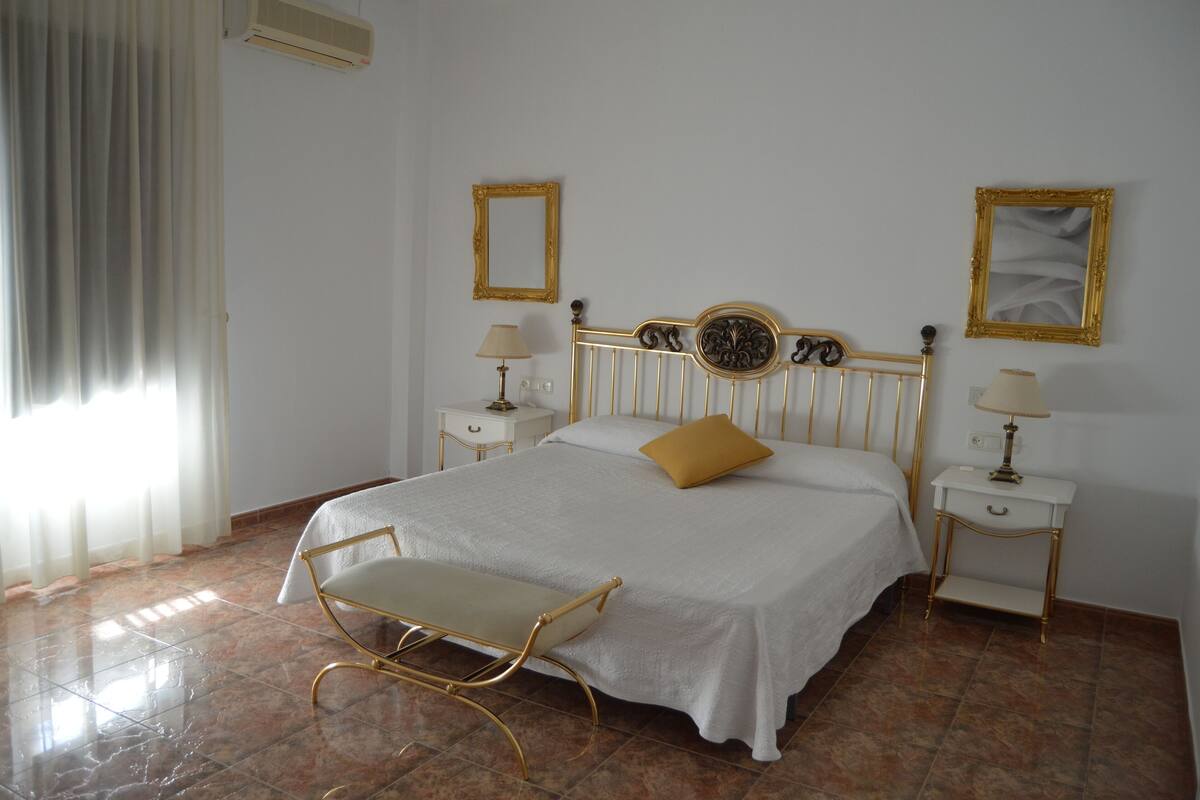 A bedroom with a bed, bedside tables, lamps, a chair, and curtains.