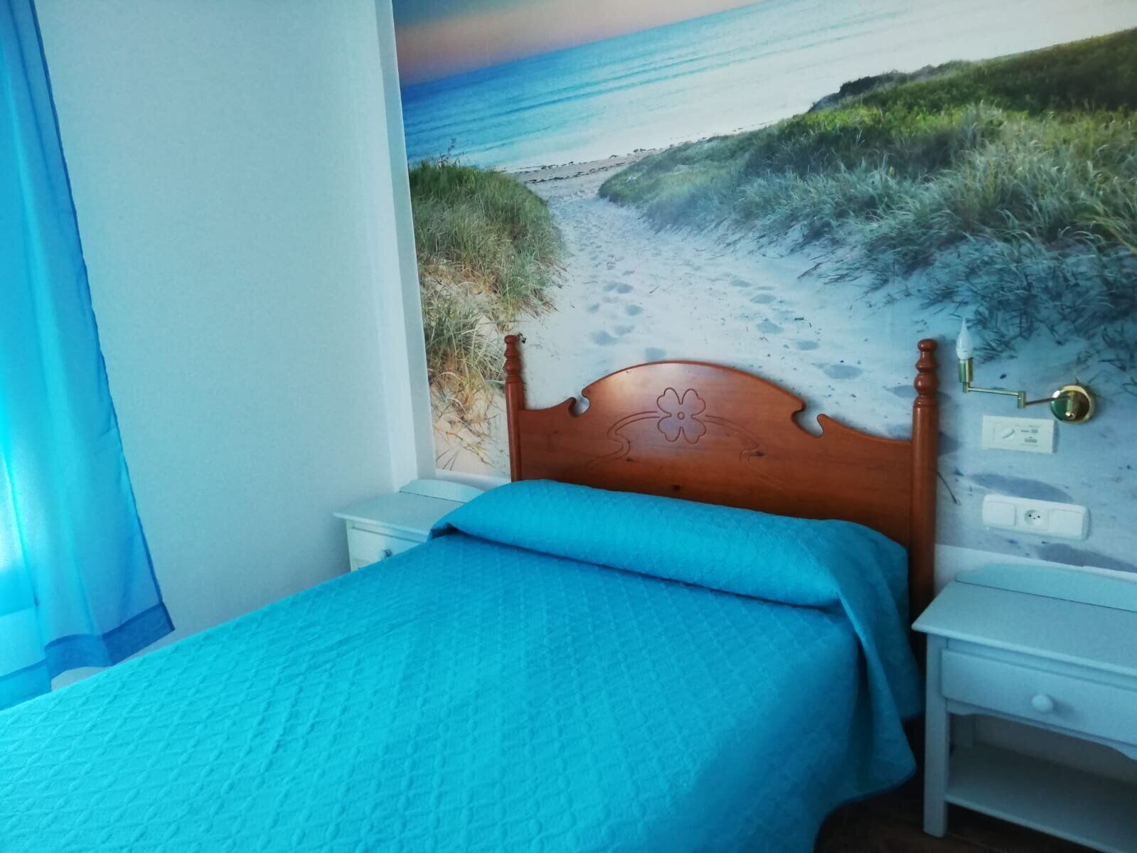 Une chambre à coucher comprenant un lit, une table de chevet, une lampe fixée au mur et une prise de courant.